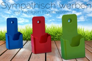 Werben Sie sympathisch - mit farbigen Prospektständern! Auf der Abbildung sind drei Prospektständer zu sehen, die nebeneinander leicht versetzt auf Holzdielen platziert sind. Die Dielen sind unter freiem Himmel und im Hintergrund ist eine Wiese angedeutet. Der linke Prospektständer ist in mittelblau gehalten, der mittlere in rot und das rechts positionierte Werbedisplay ist moosgrün. Wie eine Studie belegt, stehen diese Farben für den Wert "Sympathie" und wird bewusst fabpsycholoisch in Werbemaßnahmen eingesetzt.